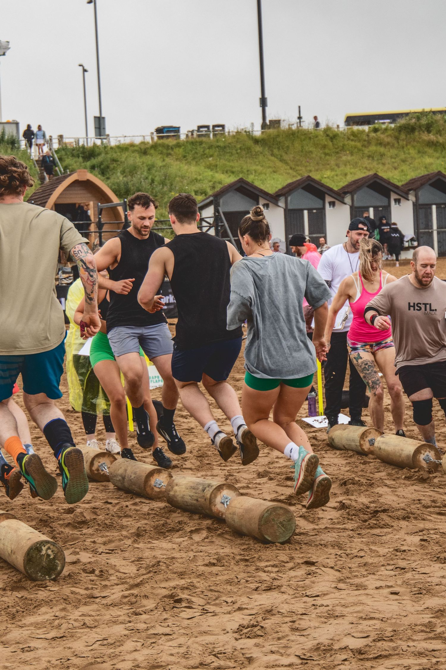 A group of participants climb over large wooden logs during a challenging outdoor obstacle course race.