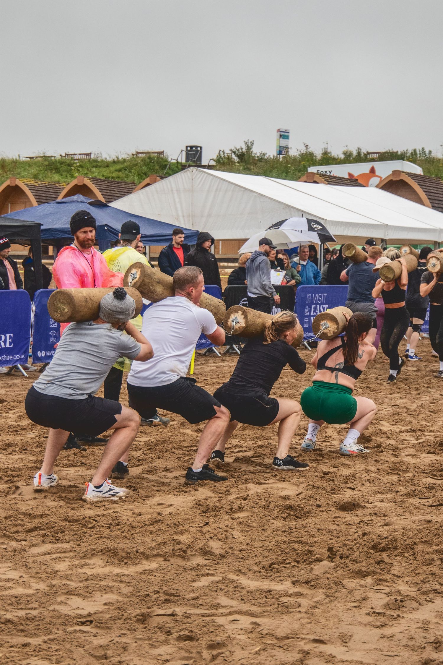 A group of participants perform synchronized squat exercises outdoors on sandy ground during an outdoor fitness event.