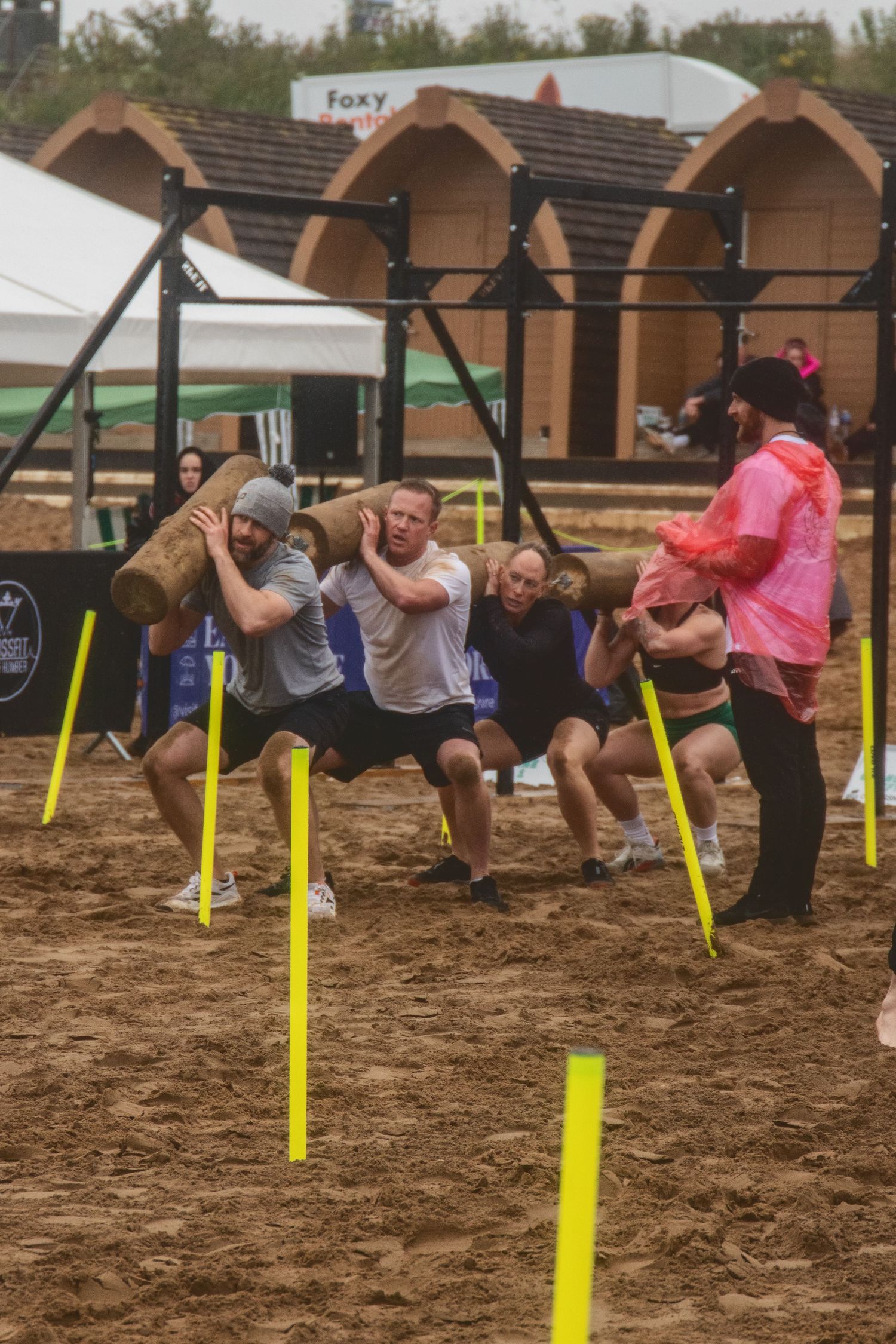 Athletes competing in a muddy obstacle course navigate under low-hanging bars during an endurance race event.