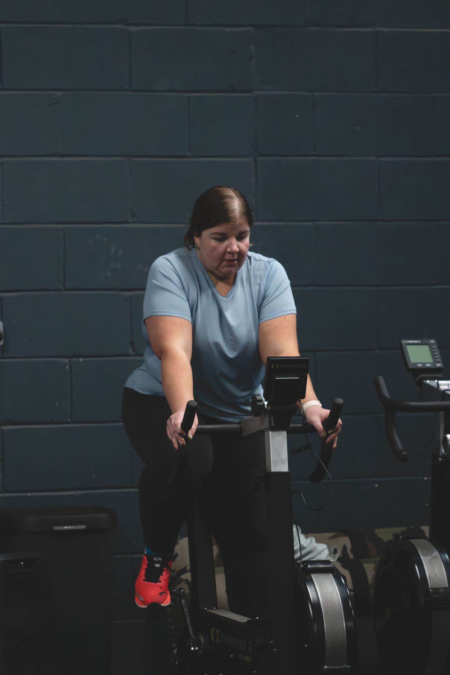 Person in gray t-shirt works out on exercise equipment against dark wall.