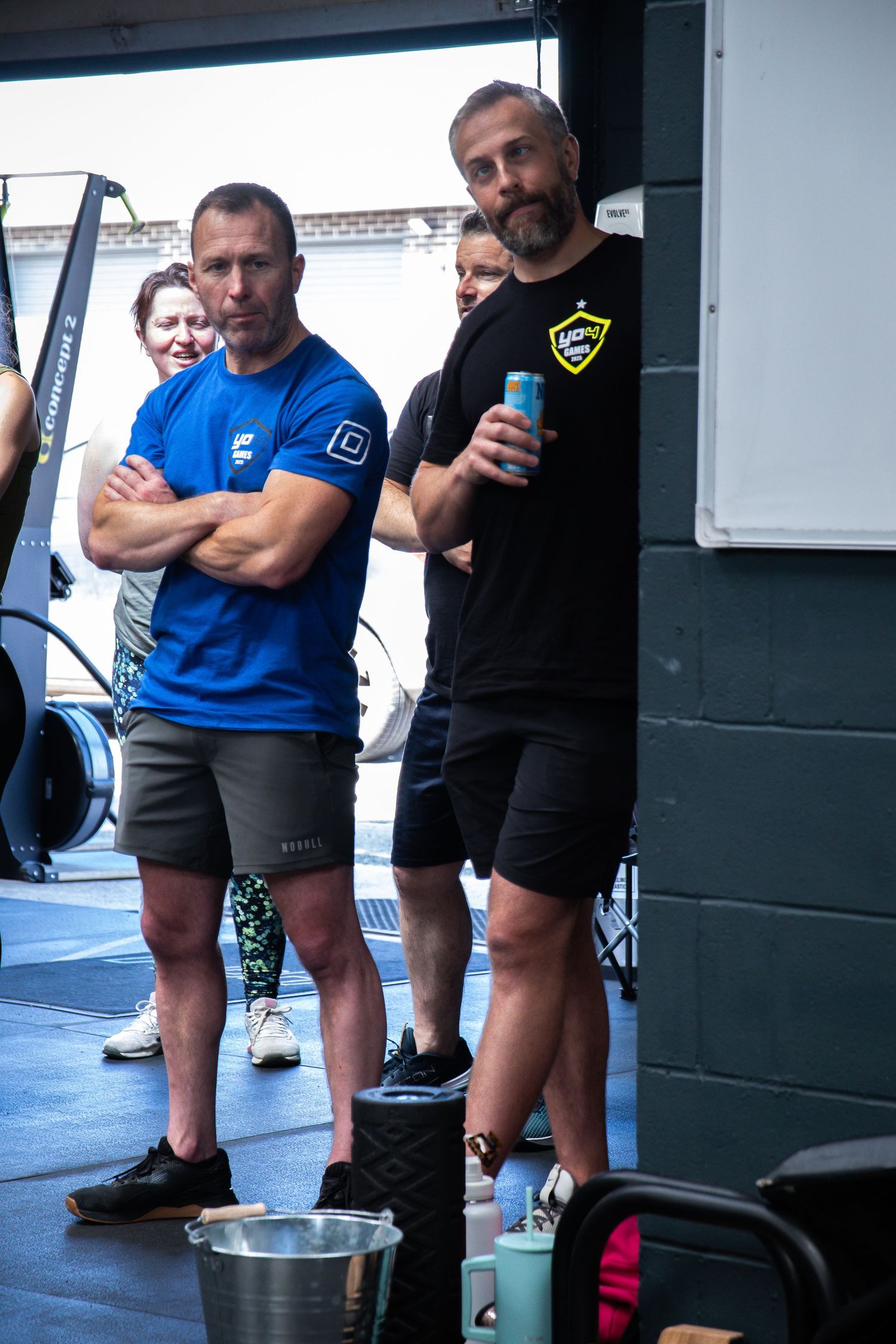 Athletes stand in a gym wearing workout clothes with exercise equipment visible in the background.
