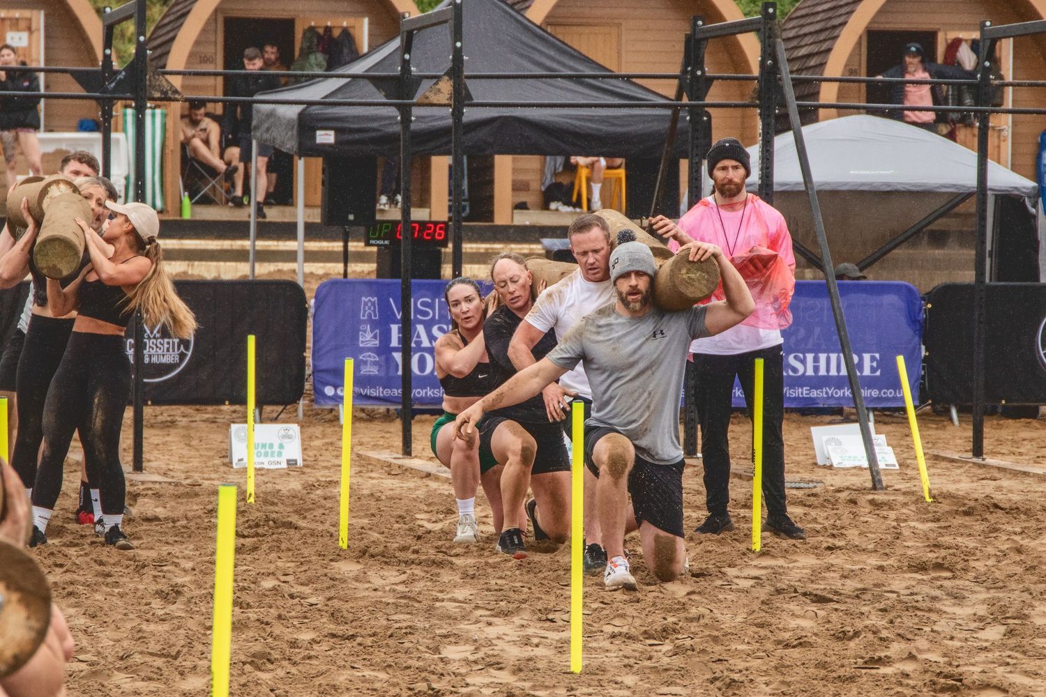 Group of people competing in an outdoor beach volleyball game on sandy court with yellow line markers and tents.