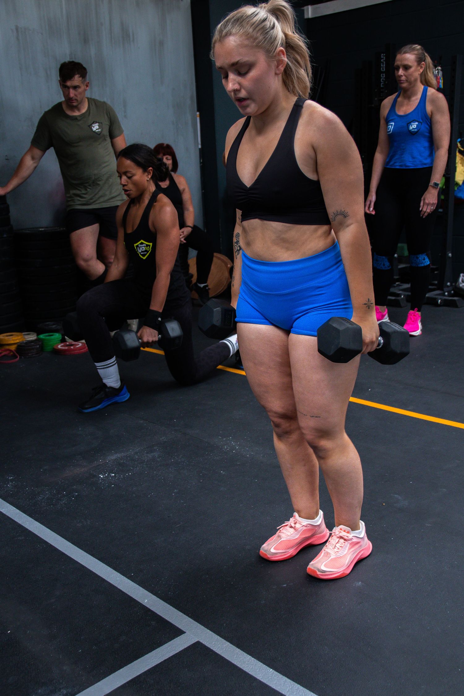 Athletes during a workout session in a CrossFit gym with dumbbells and exercise equipment.