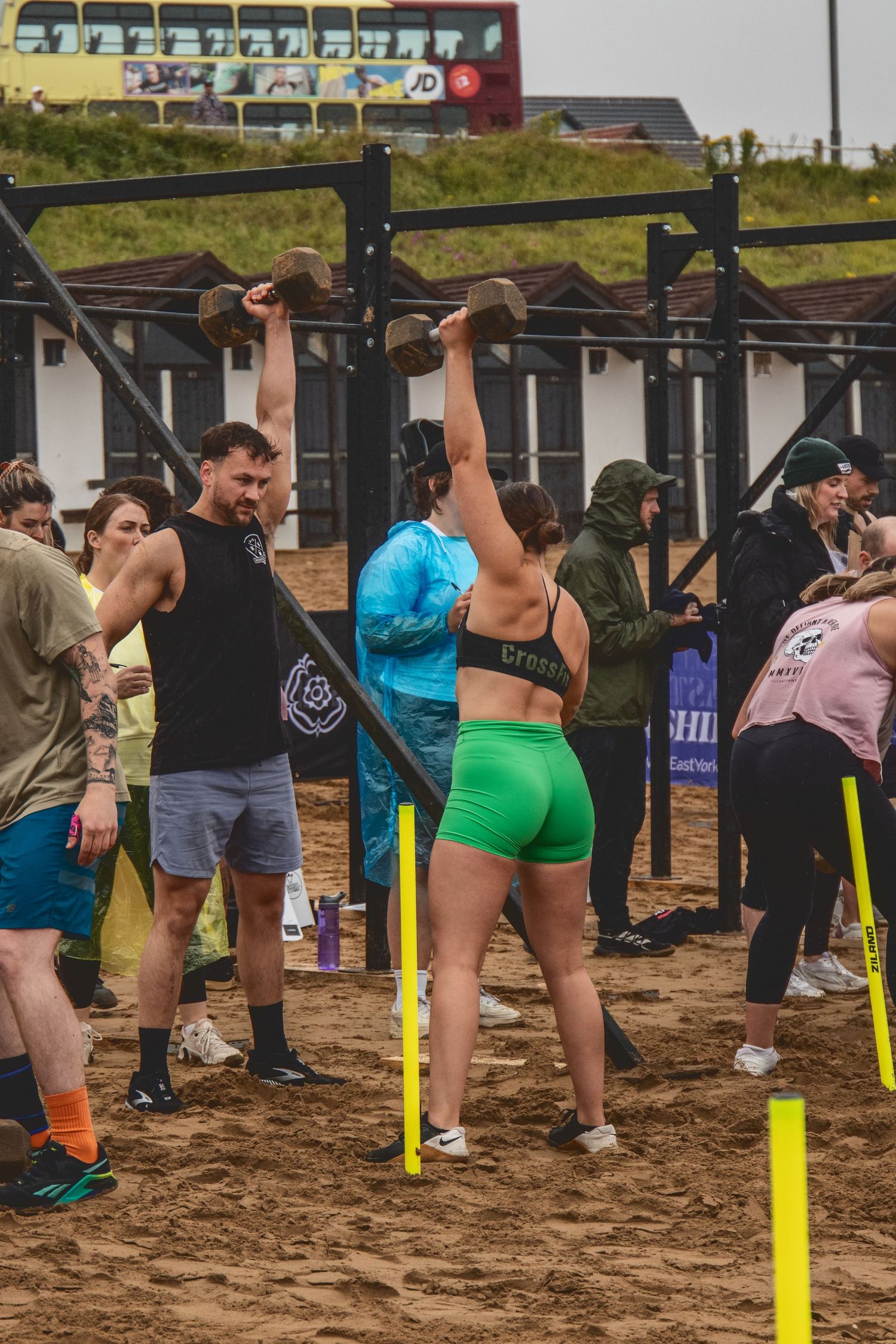 Group of people lined up outdoors participating in an exercise class on sandy ground with yellow markers.