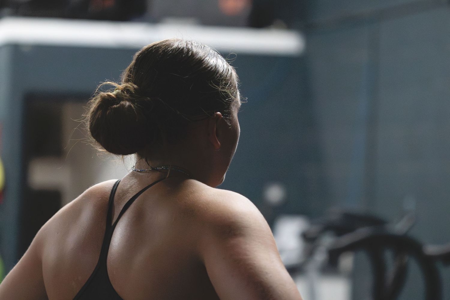 Athletic person with hair in bun viewed from behind during workout in darkened gym setting.