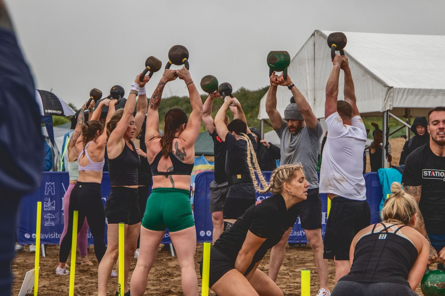 Athletes perform synchronized kettlebell exercises during an outdoor group fitness competition at a sports event.