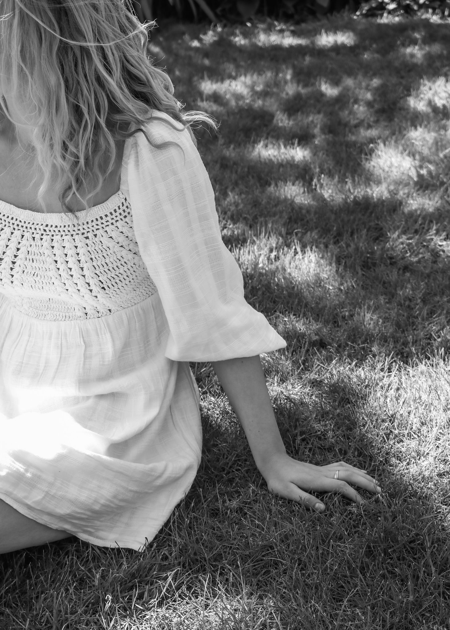 Side view of person in white lace dress sitting on summer grass.