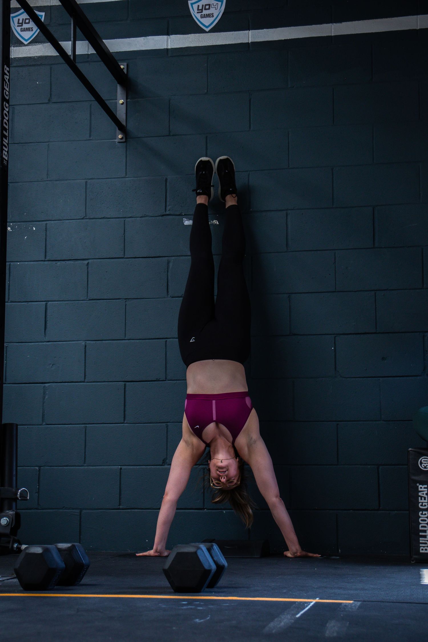 Four progressive photos show someone performing a handstand against a dark wall at what appears to be a CrossFit gym.