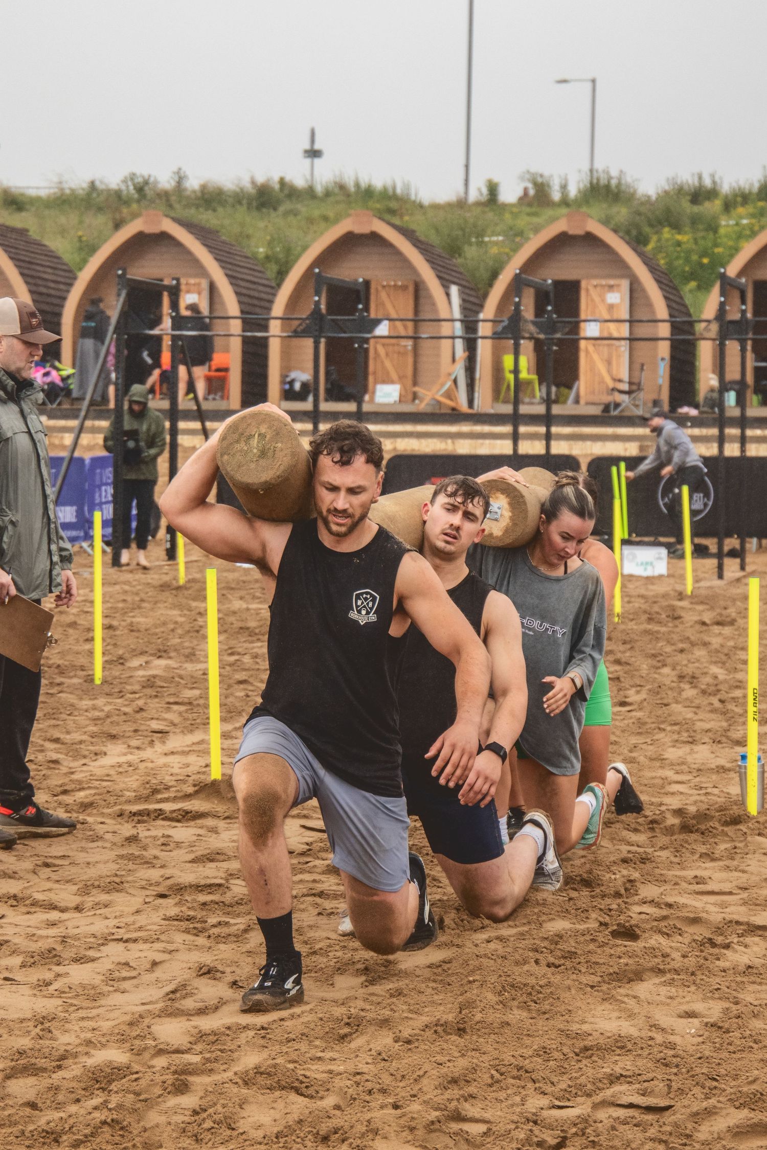 Participants navigate through obstacles in a sandy terrain race course during an outdoor fitness challenge event.
