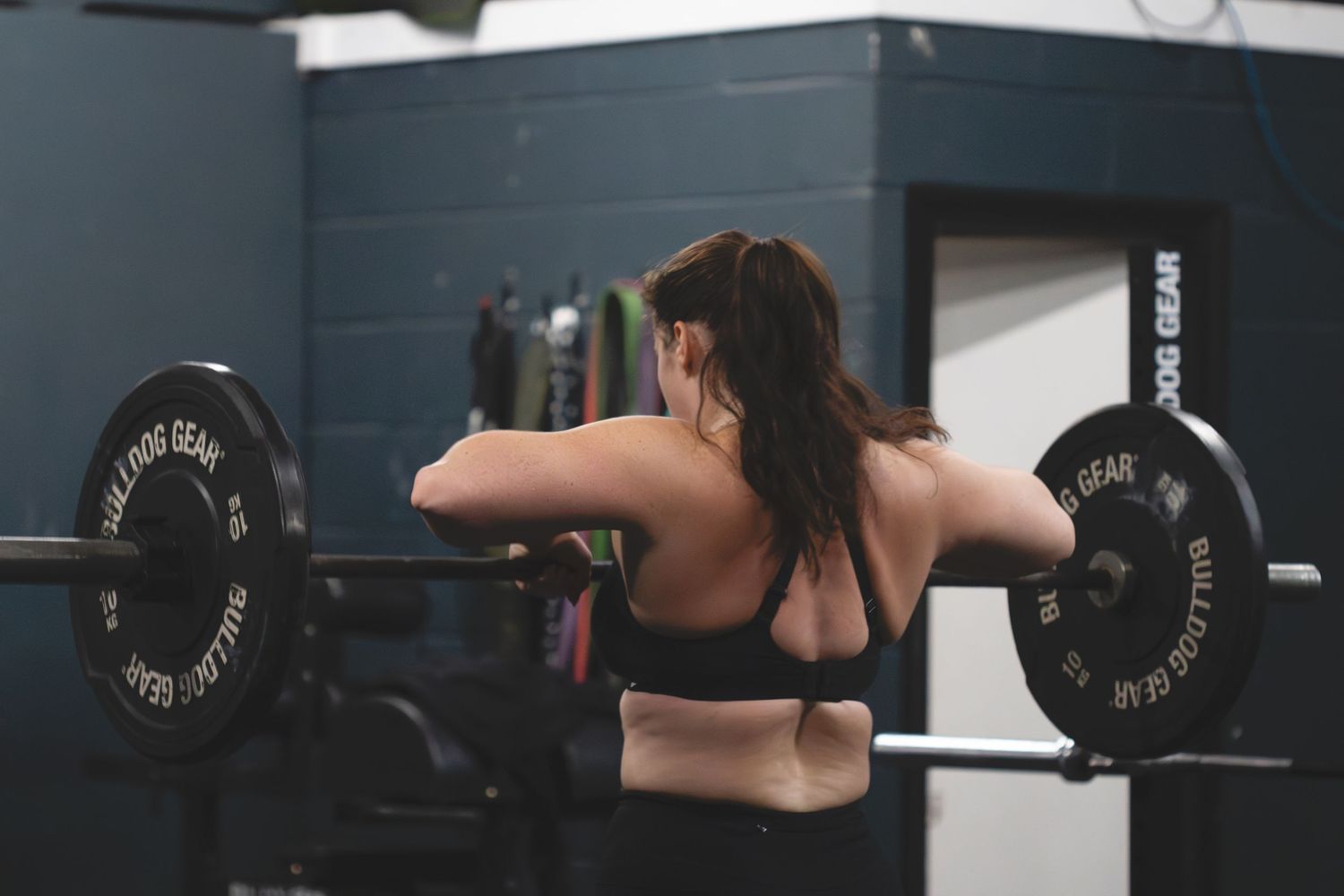 Sequence of someone demonstrating proper overhead barbell press technique in a gym setting with dark gray walls.
