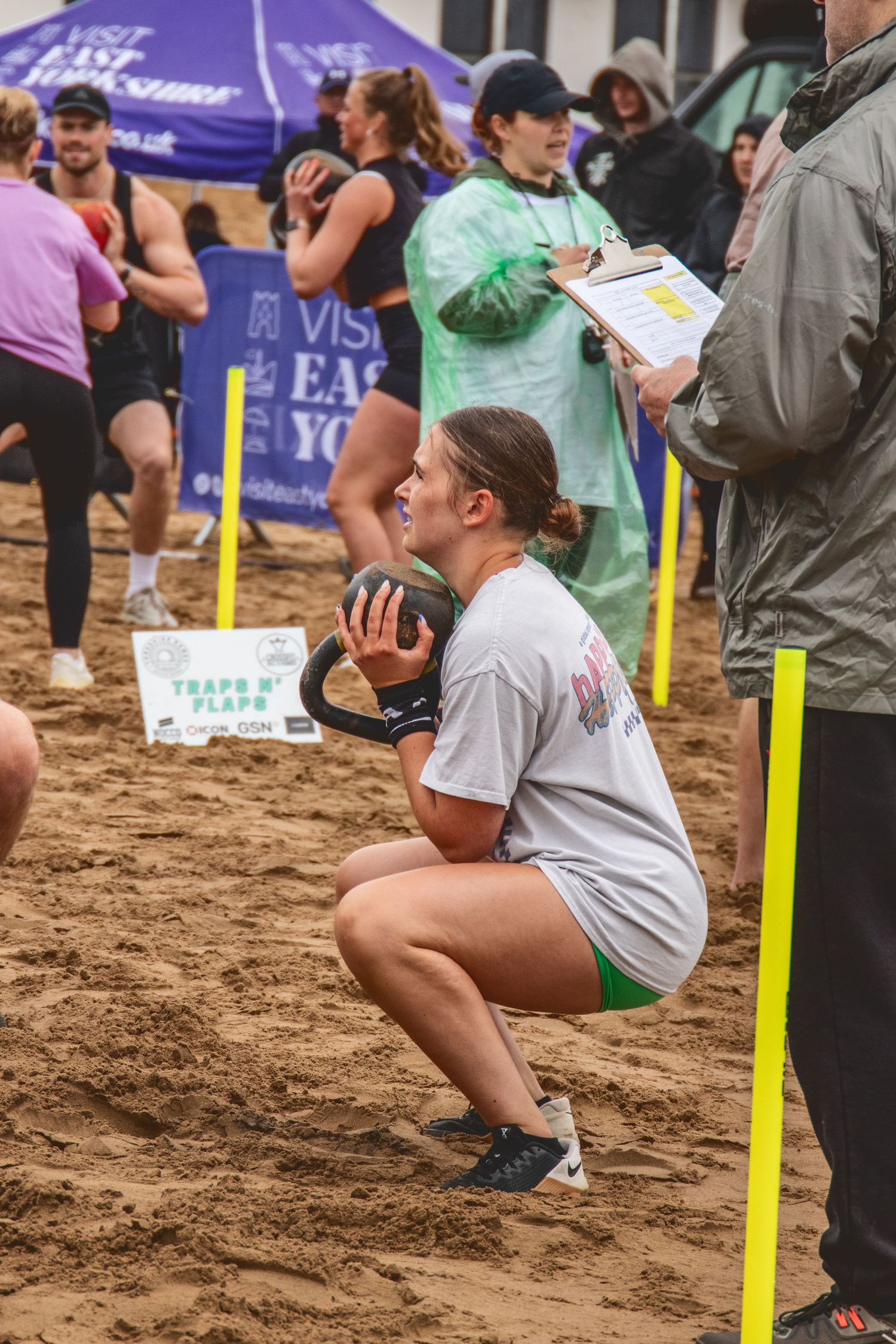 Athlete performs weighted squat exercise with medicine ball on sandy beach during outdoor fitness competition.