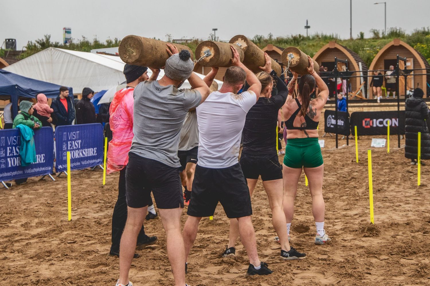 Athletes line up at a recreational volleyball tournament being held on an outdoor sand court with poles and flags visible.