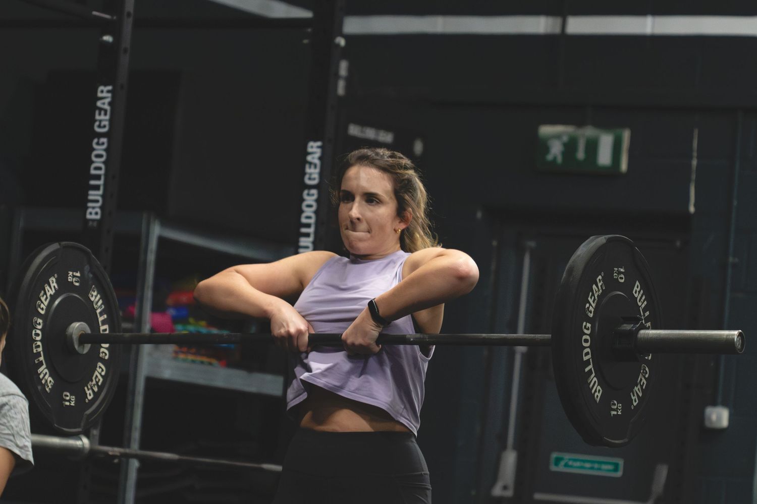 A person performs a barbell clean and press exercise at a CrossFit gym with dark lighting.