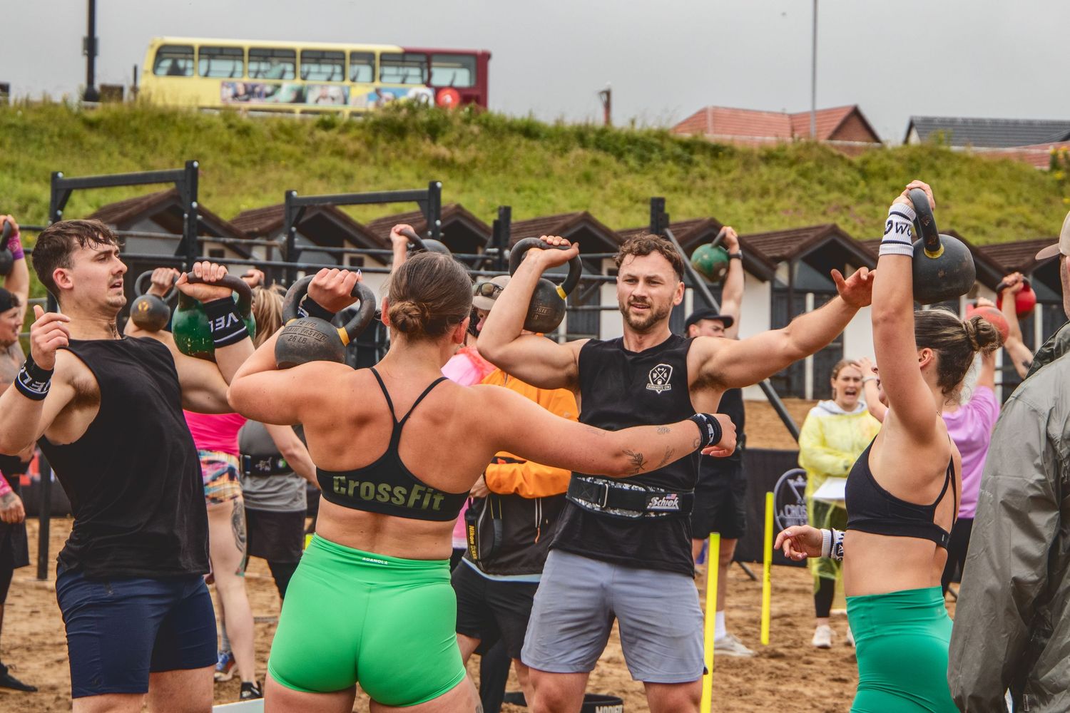 A group of athletes celebrate during an outdoor fitness competition event on a grassy field.