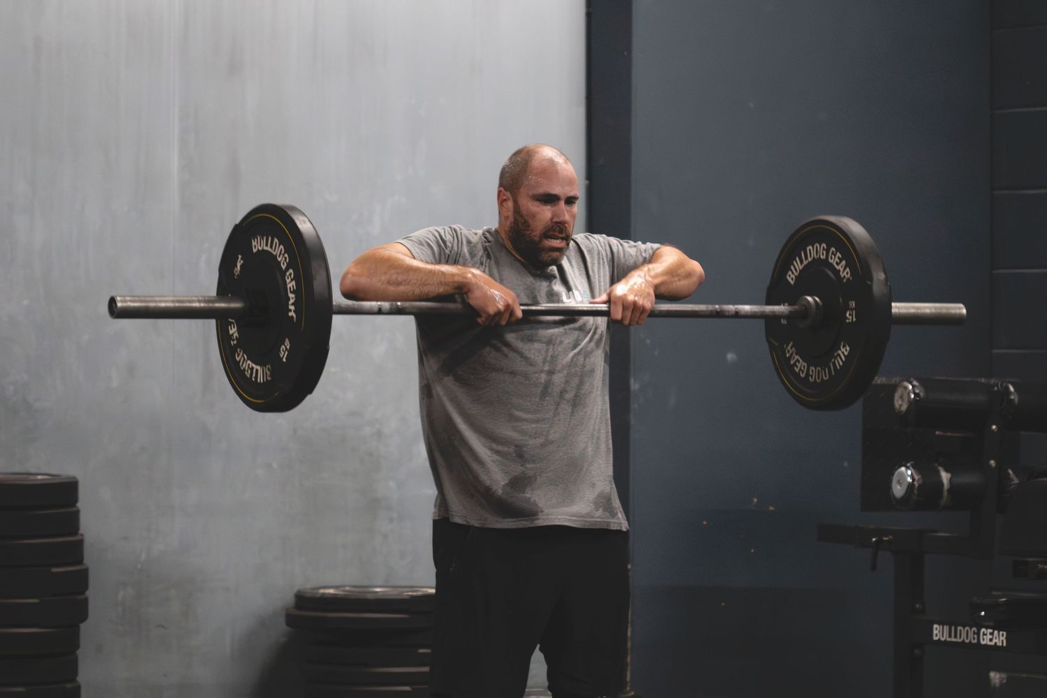 Athletic person performing a barbell lift in a dark gym with a focused expression.
