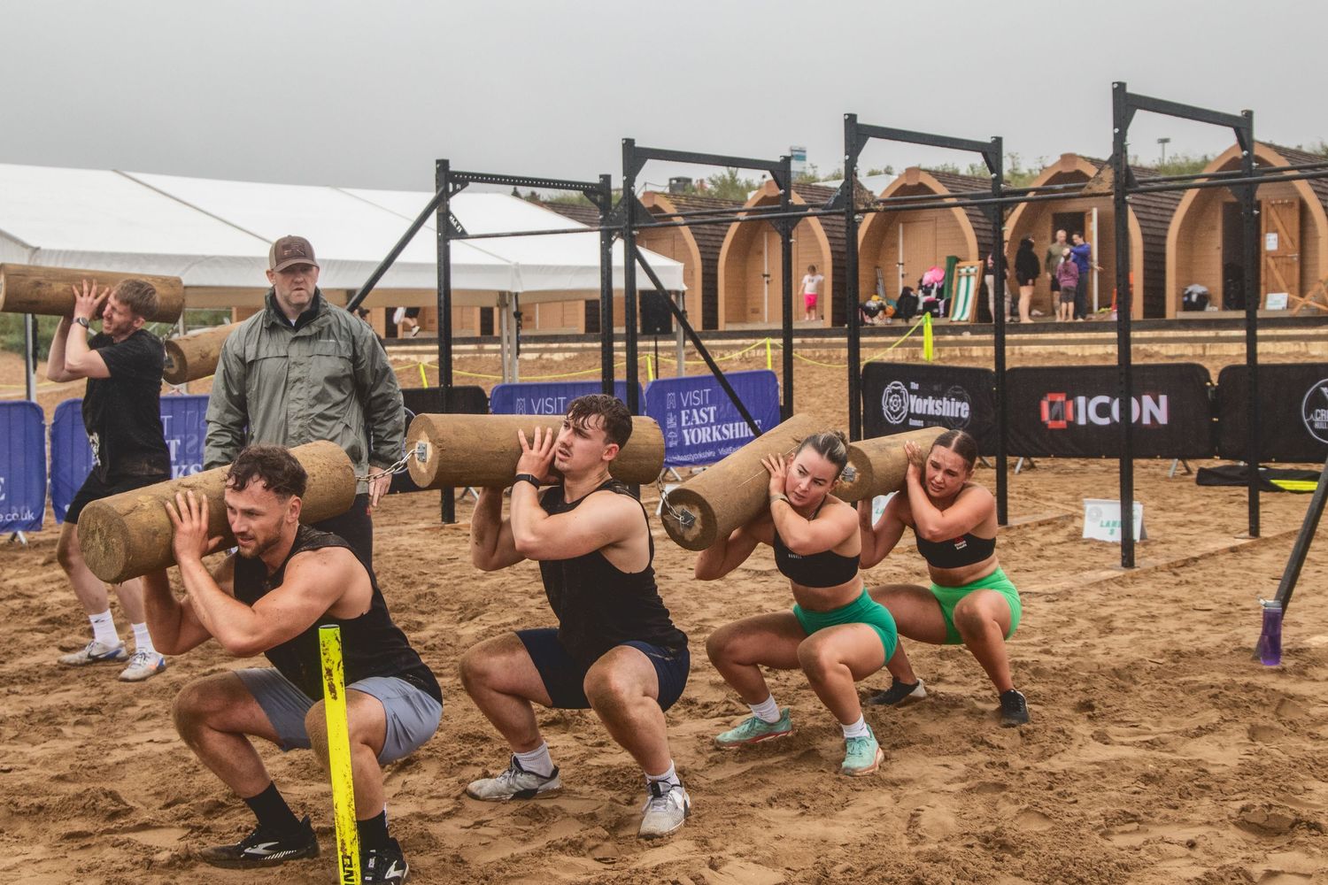Athletes perform synchronized squats with resistance bands during an outdoor CrossFit competition on sandy terrain.