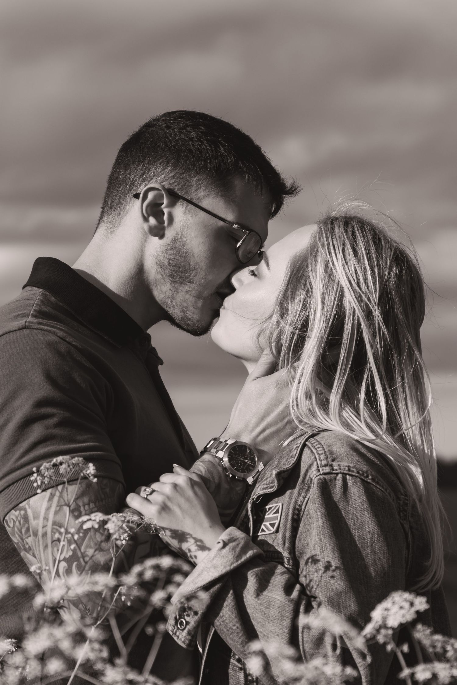 Romantic couple embraces in a wildflower field under dramatic cloudy skies.