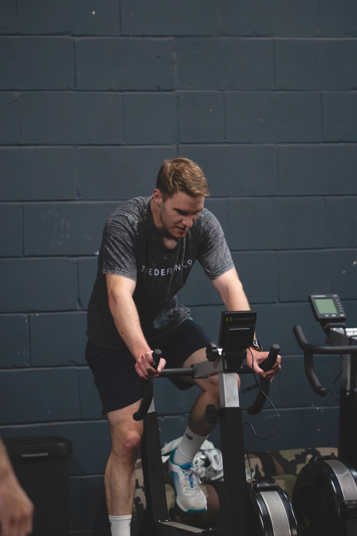 Someone exercising on a stationary bike in a dark gym setting against a grey wall.