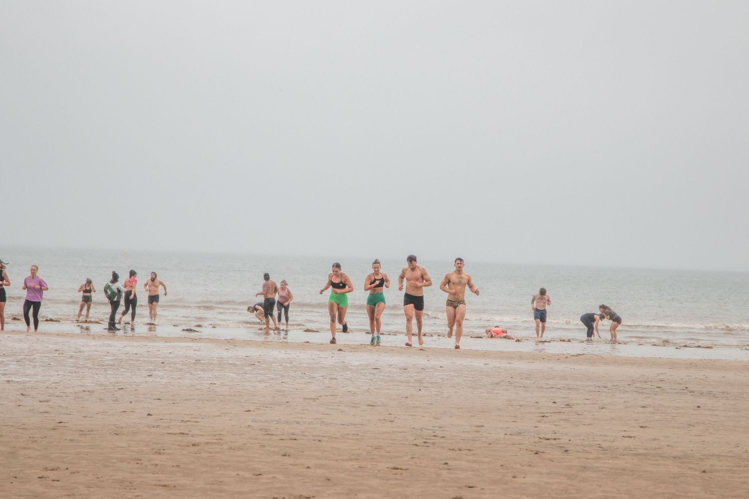 Beachgoers enjoying a misty summer day on a sandy shore with gray overcast skies in the background.