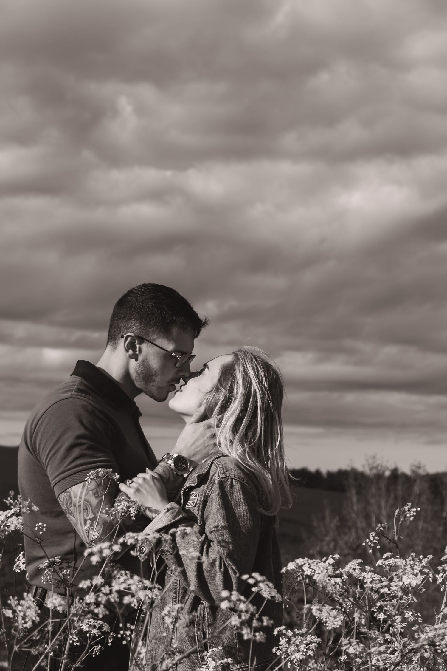 Atmospheric black and white portrait of couple's embrace amid flowering meadow.