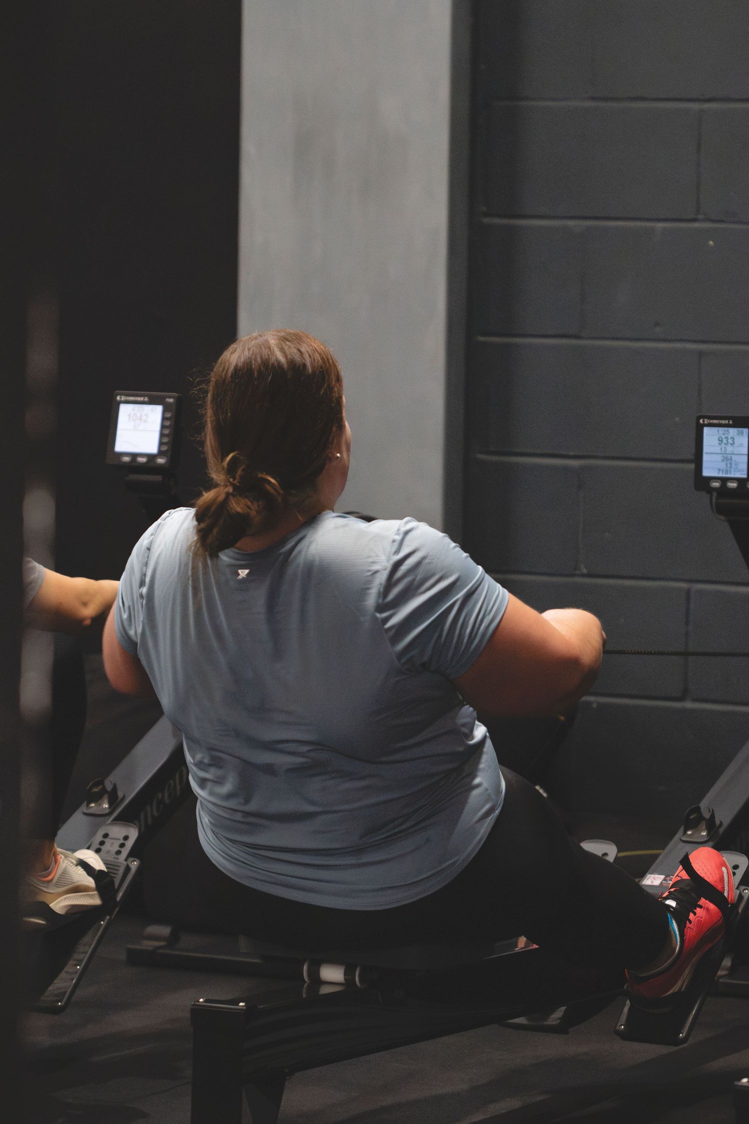 Person in grey t-shirt working out on a rowing machine at a dark gym facility.