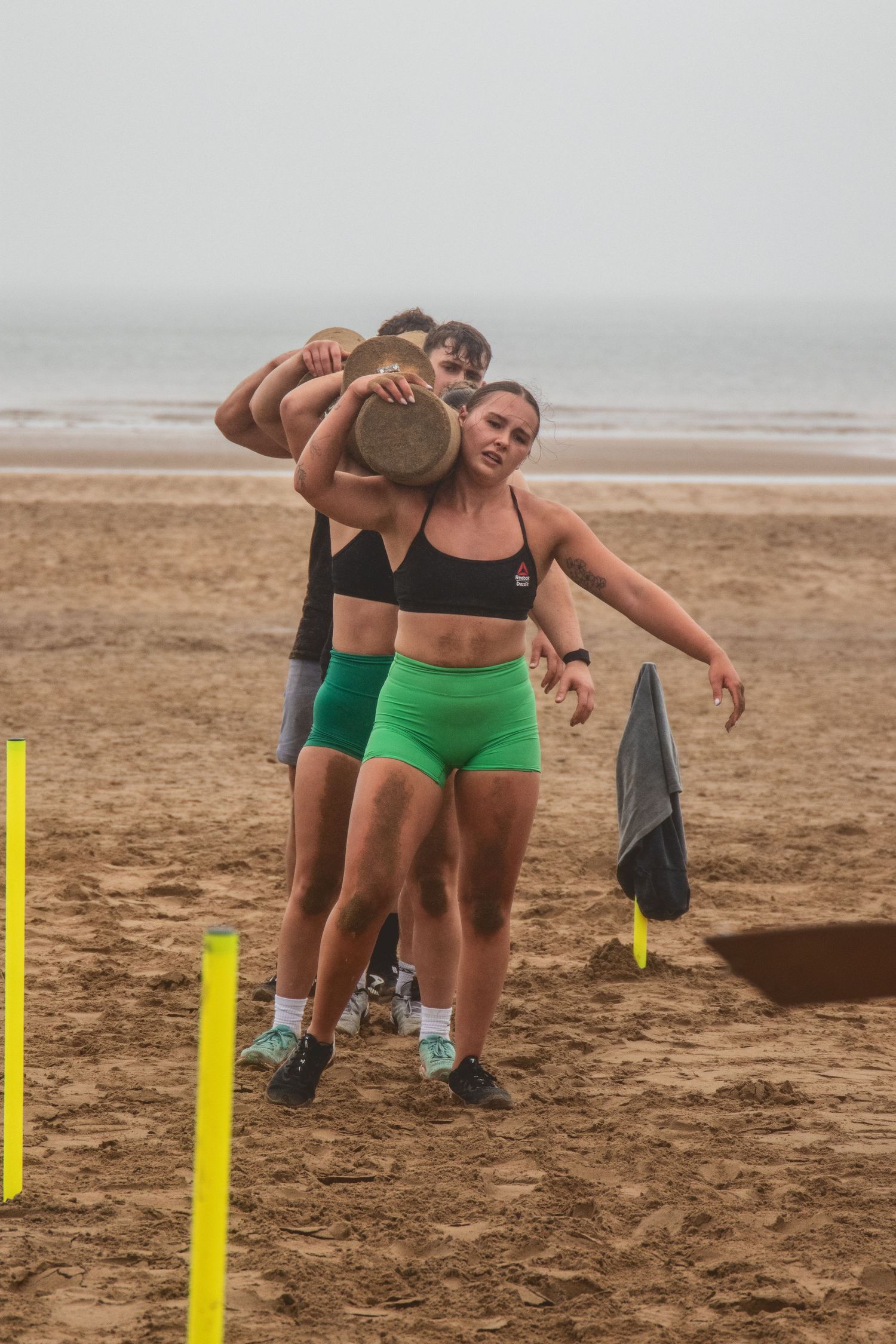 Athletes practice together during a beach training workout, digging on sand with yellow markers in the background.