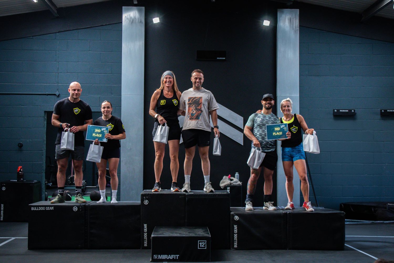 Athletes stand on competition podiums at a fitness event in an indoor gym setting.