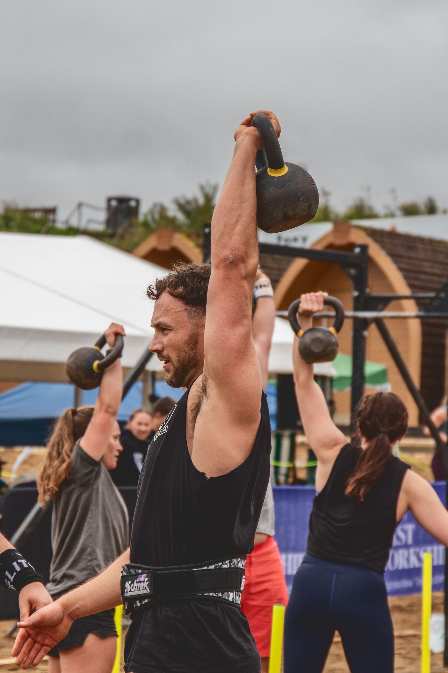 Athletes performing overhead kettlebell exercises during an outdoor fitness competition or training session.