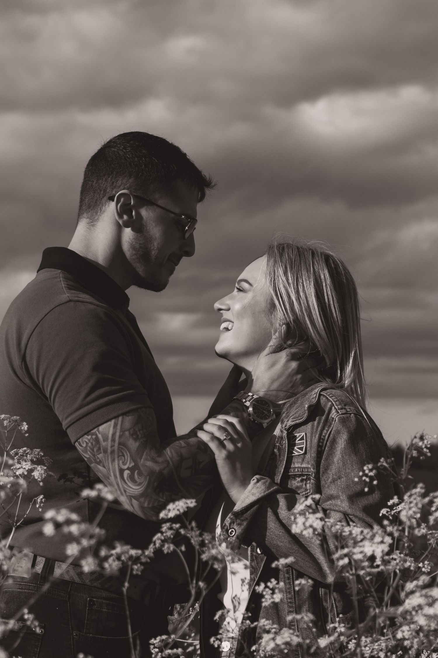 Black and white portrait of a couple in an emotional embrace among flowering meadow plants.