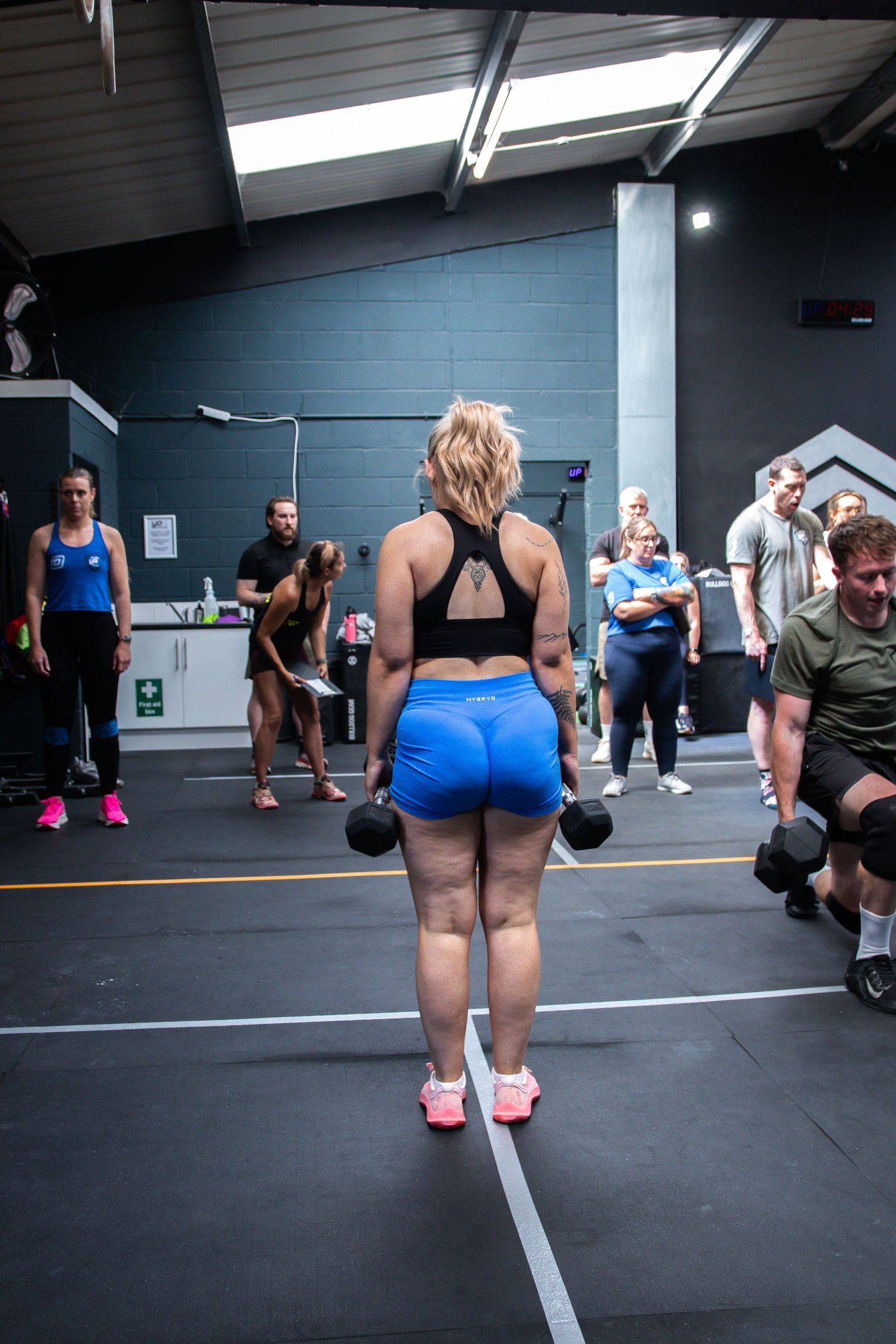 Group of people performing lunges with dumbbells during a fitness class in a modern gym.