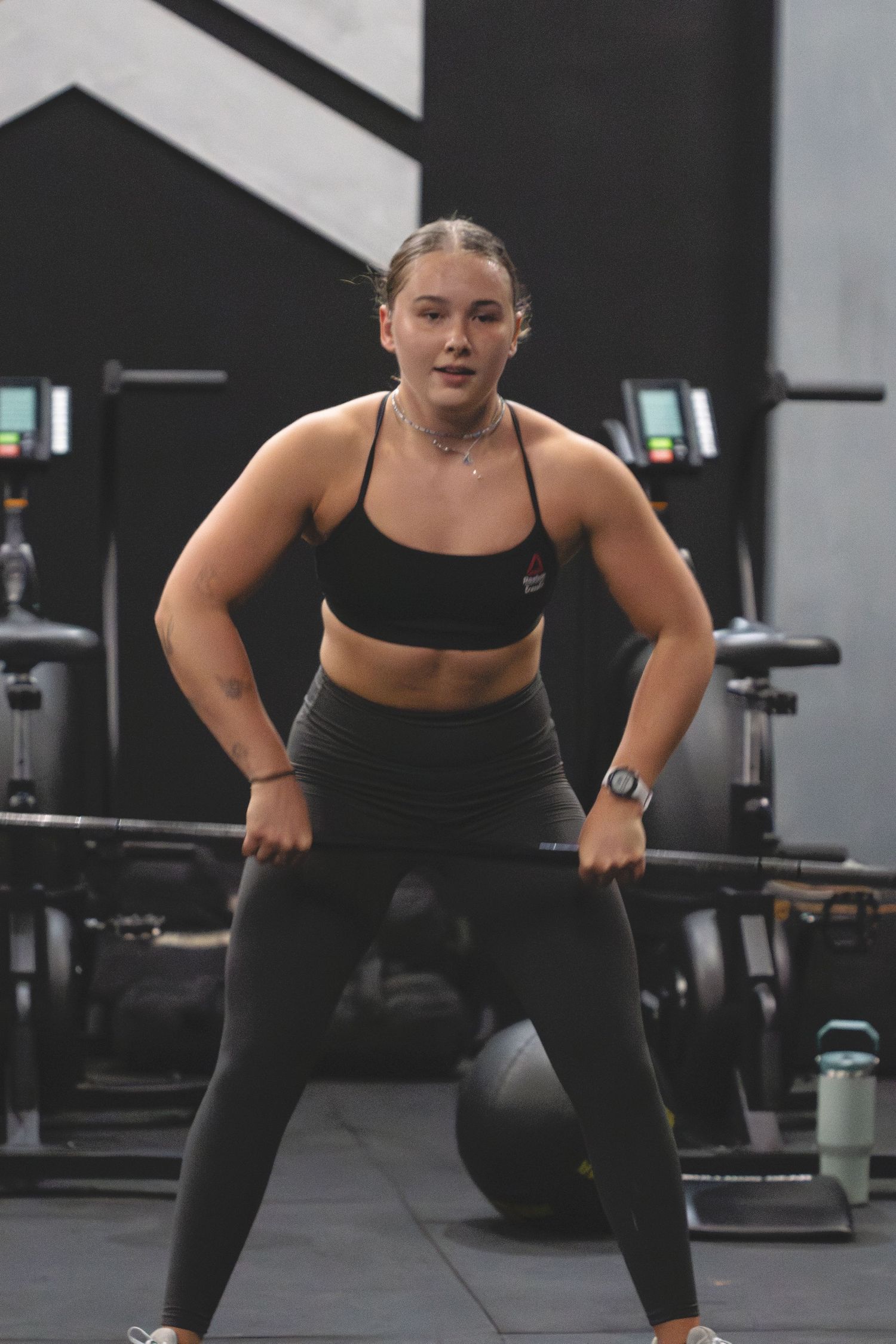 Female athlete performs dumbbell snatches during an intense CrossFit workout in a modern gym setting.
