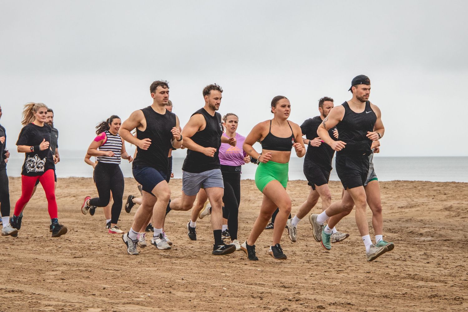 A group of fitness enthusiasts perform squat exercises together on a sandy beach during an outdoor workout session.