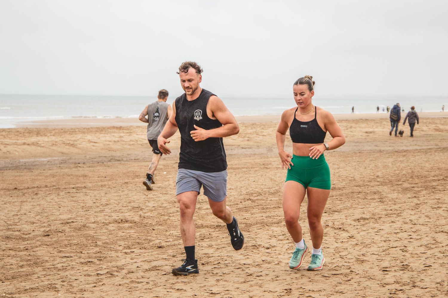 Two people jogging together on a sandy beach during an overcast day.