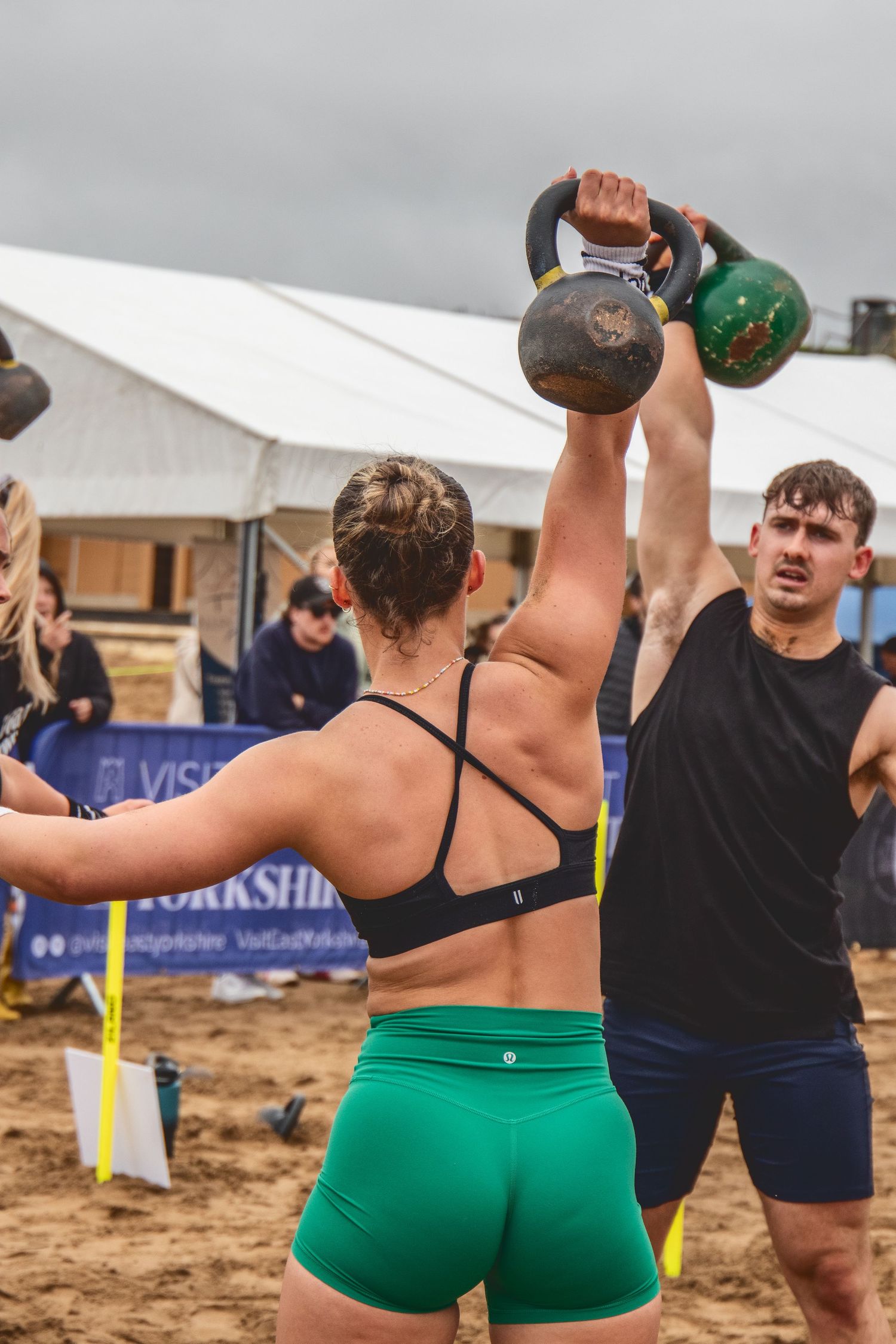 Athletes working out with kettlebells during an outdoor beach fitness competition or training event.