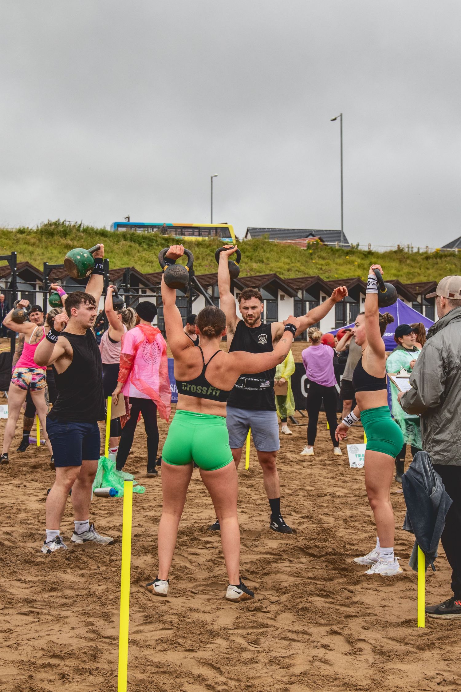 A sequence of participants playing a party game with limbo poles on a sandy beach during an outdoor event.