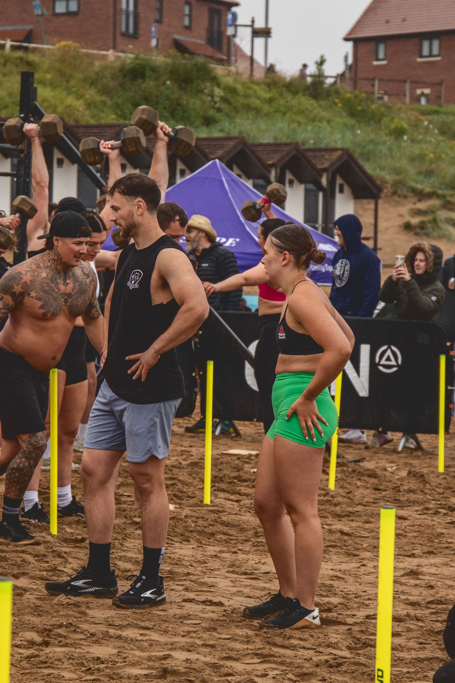 People lined up in a row bend over to participate in an outdoor fitness competition on dirt ground.