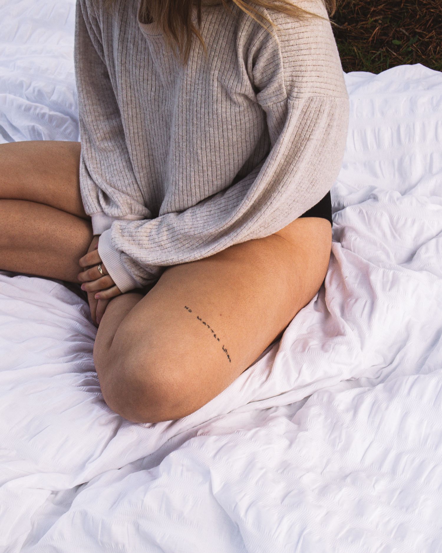 Close-up of arms resting on white bedding showing a small tattoo.