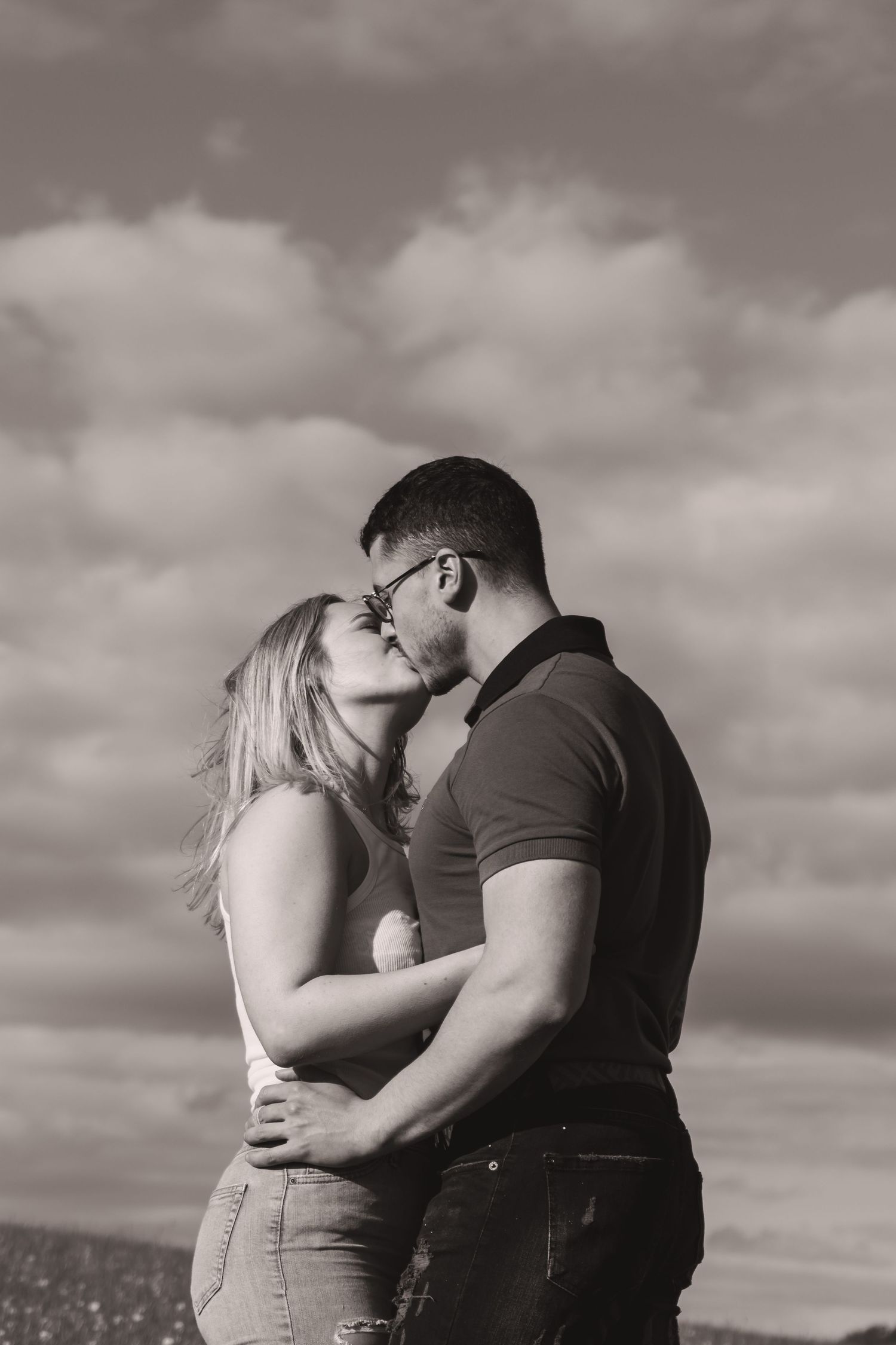 Sepia-toned romantic portrait of couple embracing under cloudy skies.