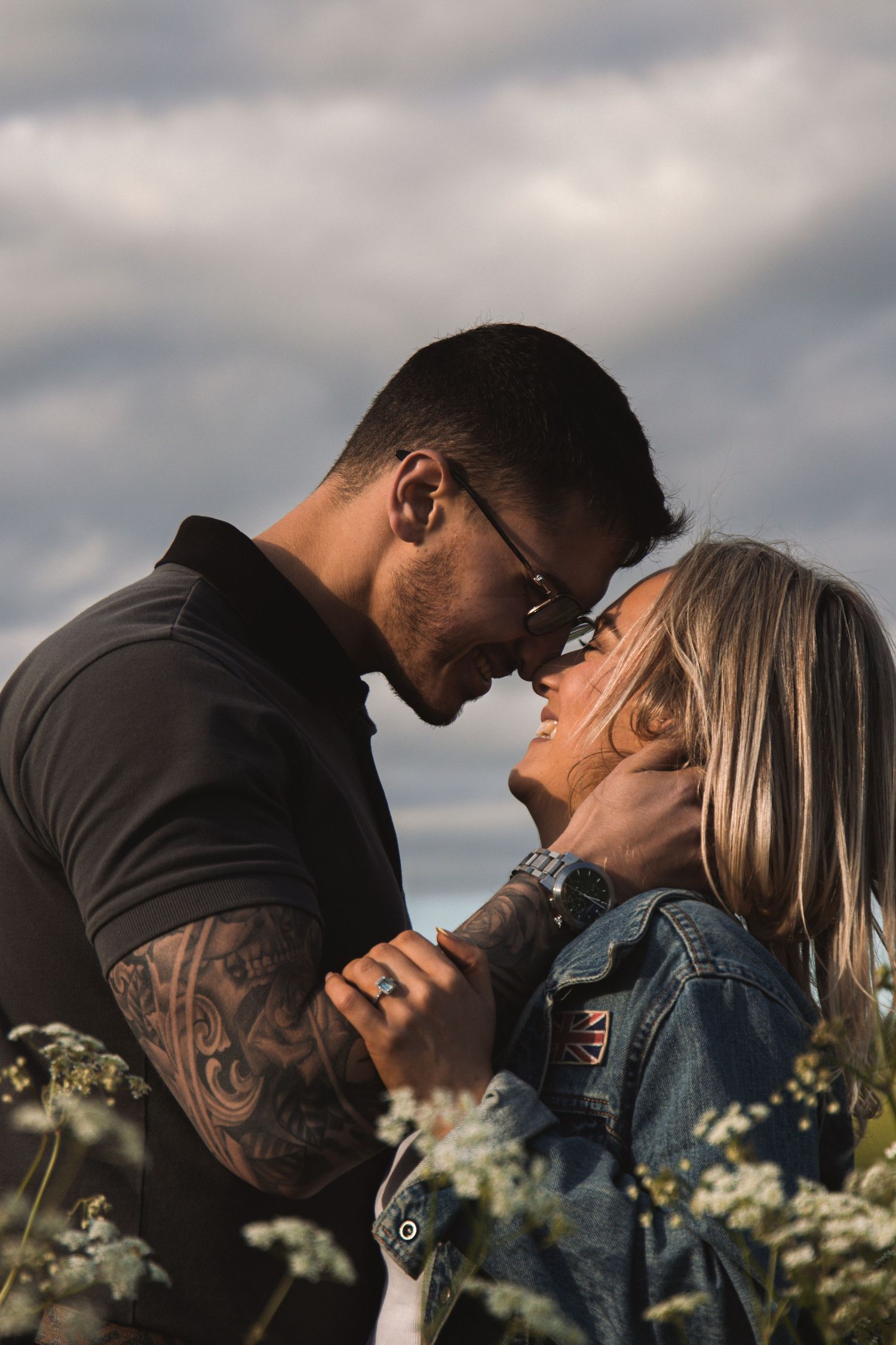 Romantic couple sharing an intimate moment among wildflowers under dramatic cloudy skies.