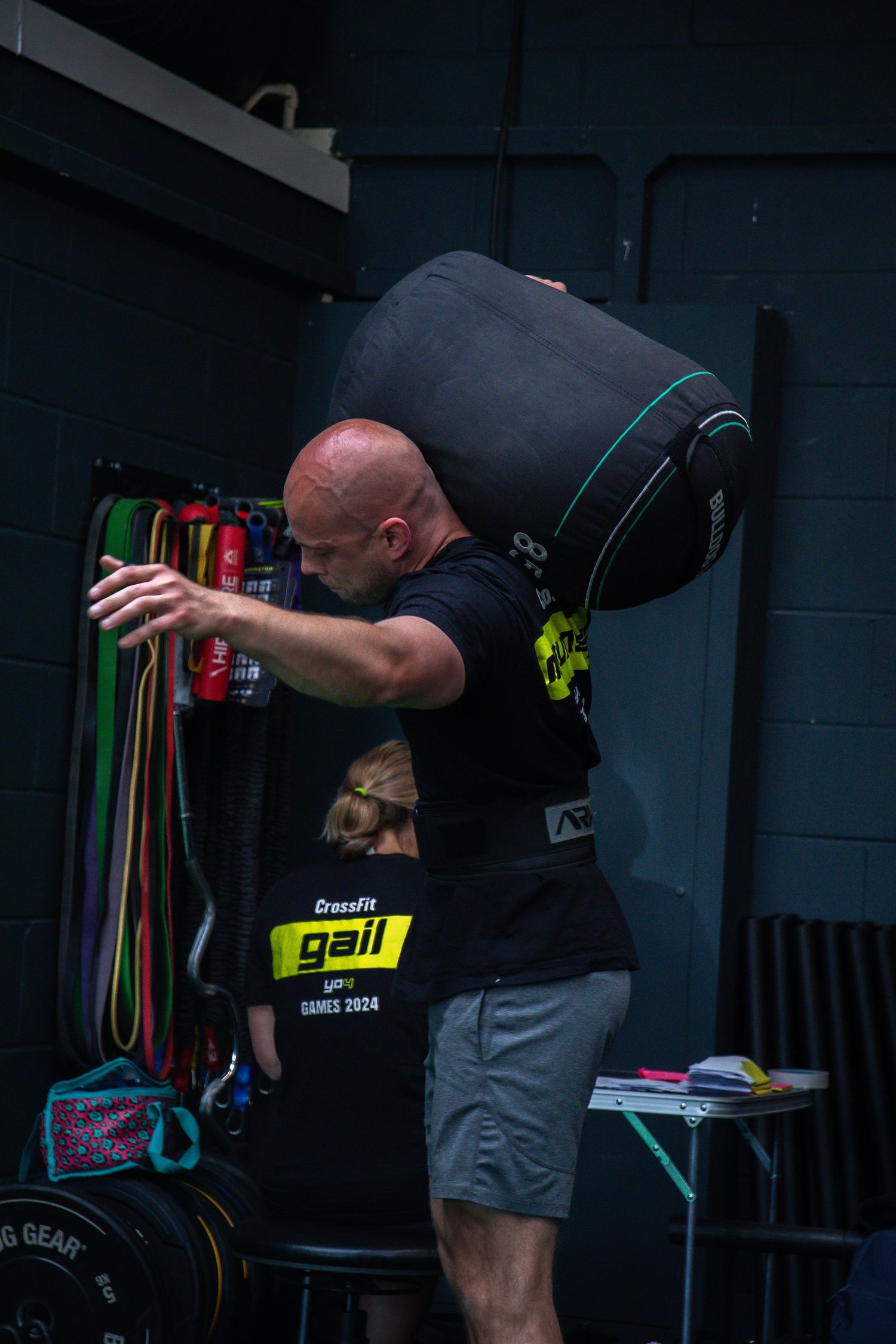 A CrossFit athlete wearing a black t-shirt prepares equipment with resistance bands in a dark gym setting.