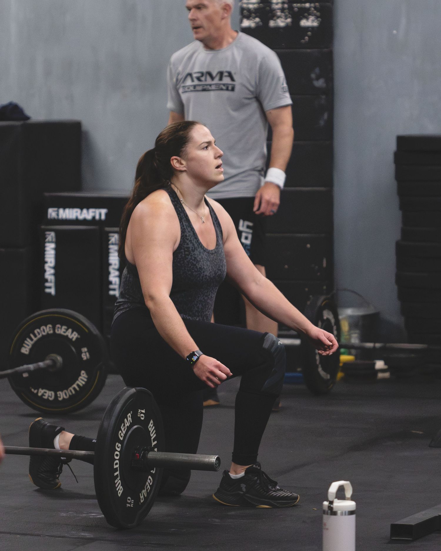 Athlete performing a deadlift exercise with barbell weights in a CrossFit-style gym setting with black equipment.