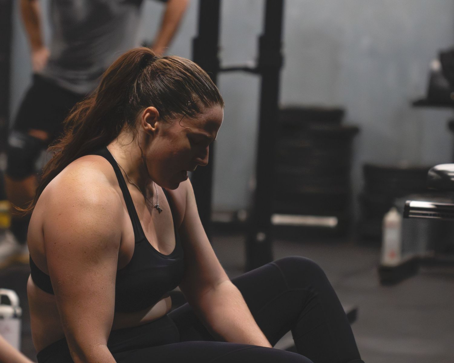 An athletic person in exercise attire rests between sets at a dimly lit gym during a workout session.