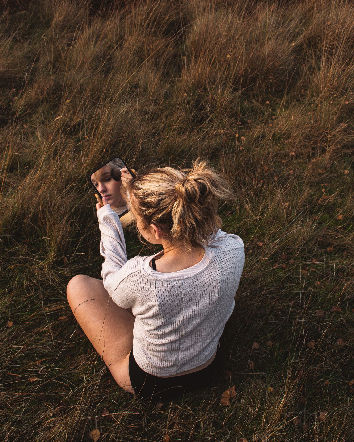 Person in gray sweater sitting in tall autumn grass during golden hour.