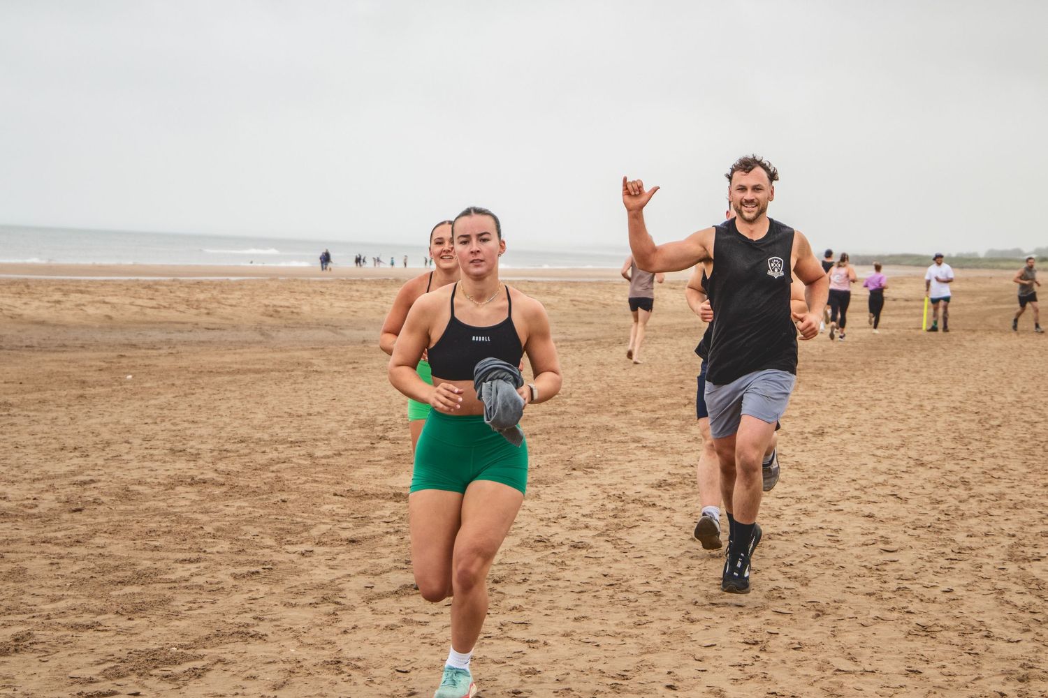 Runners enjoying a beach race along the sandy shoreline on an overcast day.