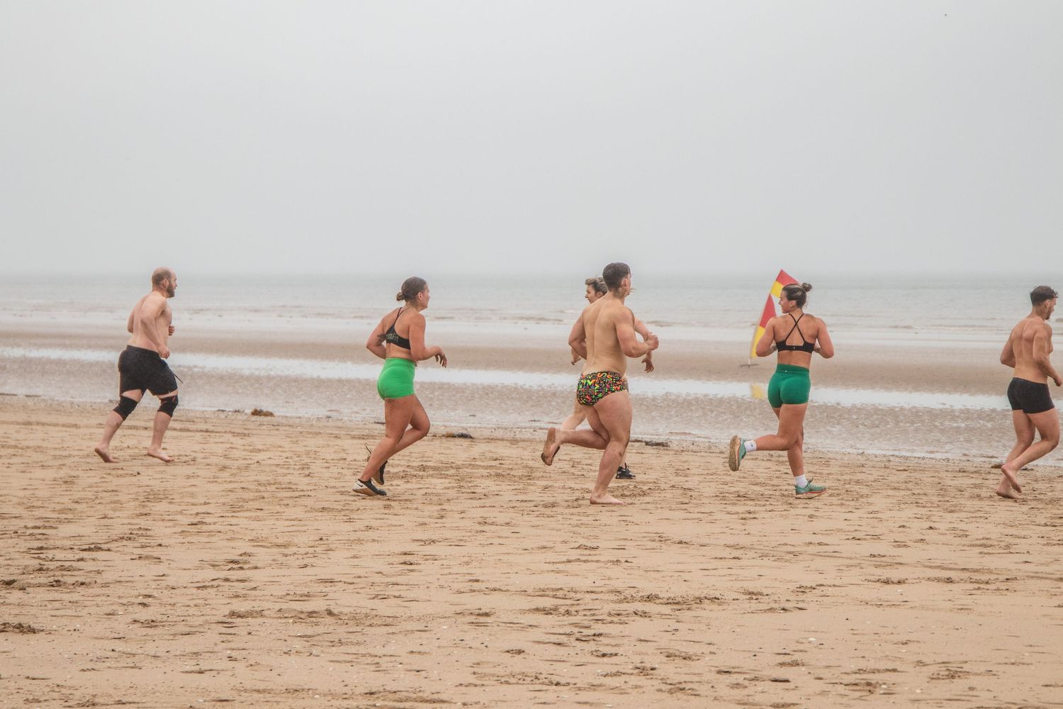 A group of runners jog along a misty beach shoreline in fitness clothing.