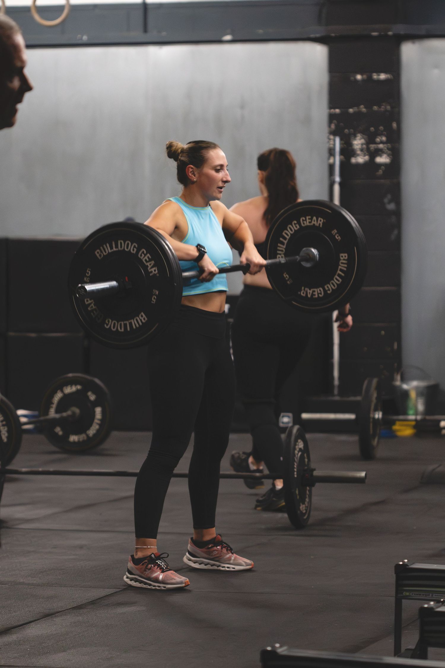Athletic person in blue sports top and black leggings performing a barbell lift during CrossFit workout at a gym.