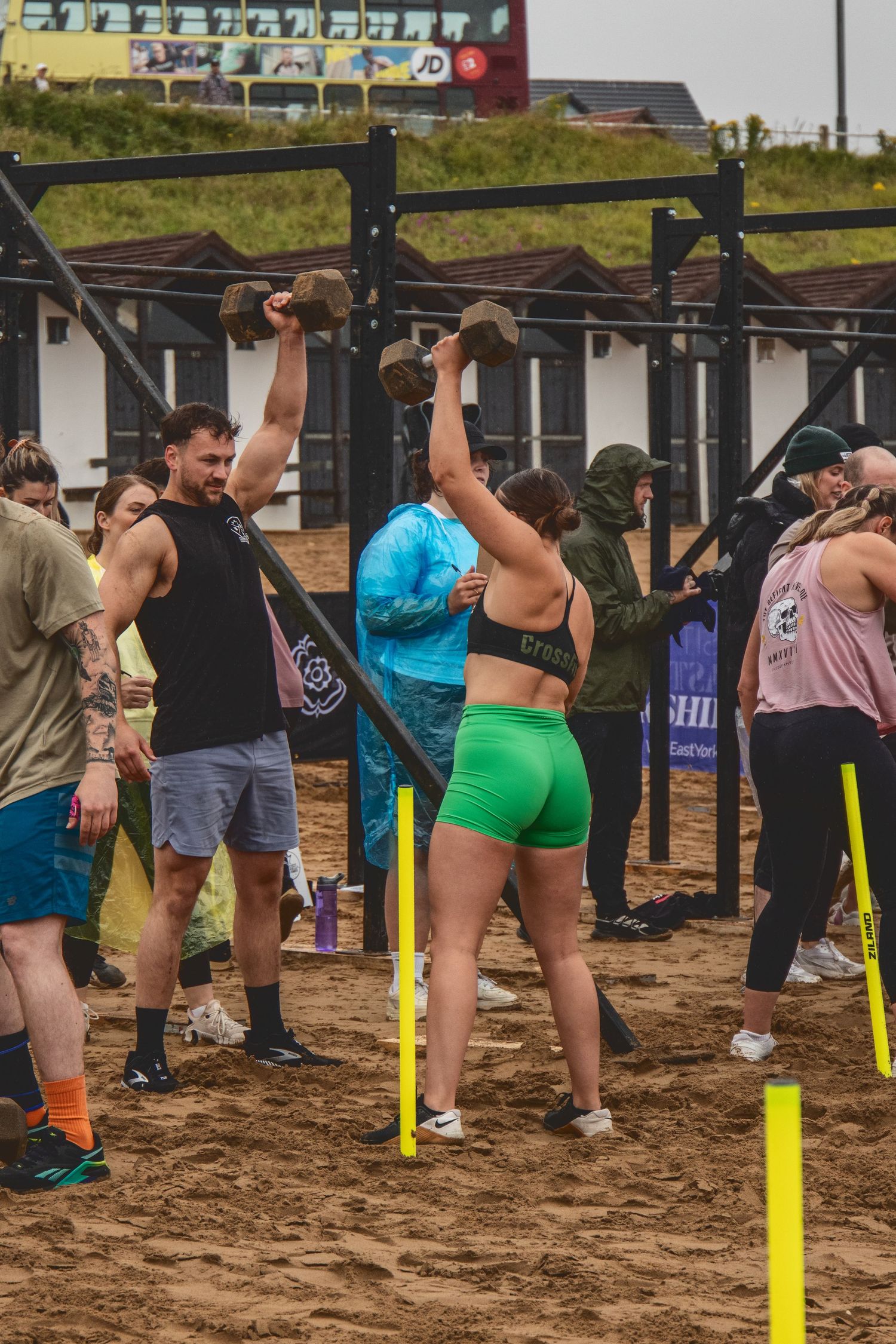 Athletes practicing pull-ups on outdoor fitness equipment during a CrossFit-style workout competition on sandy ground.