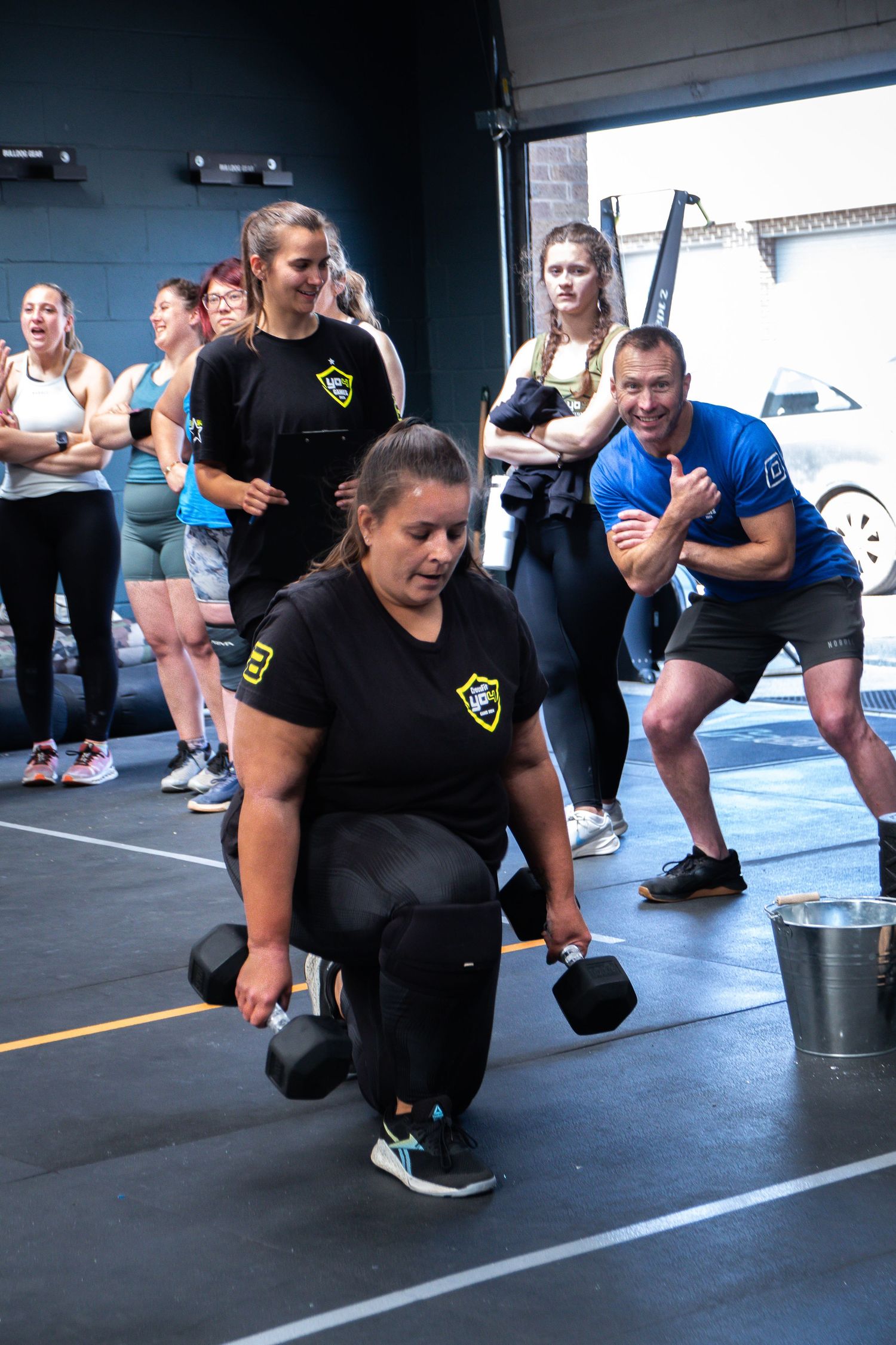 A group of athletes perform dumbbell exercises during an intense CrossFit training session in a gym.