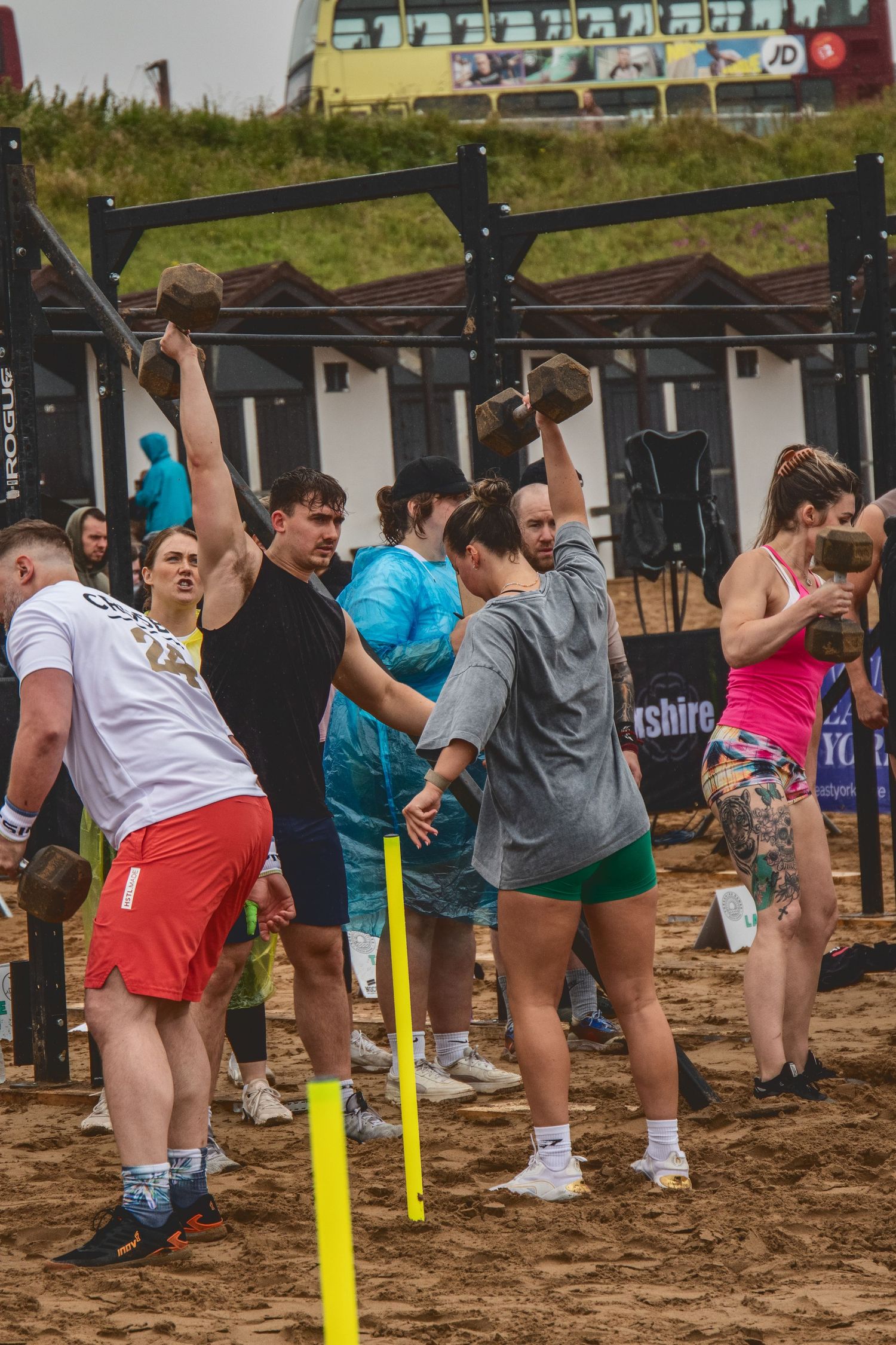 Athletes training and exercising at an outdoor CrossFit competition area with exercise equipment and pull-up bars.