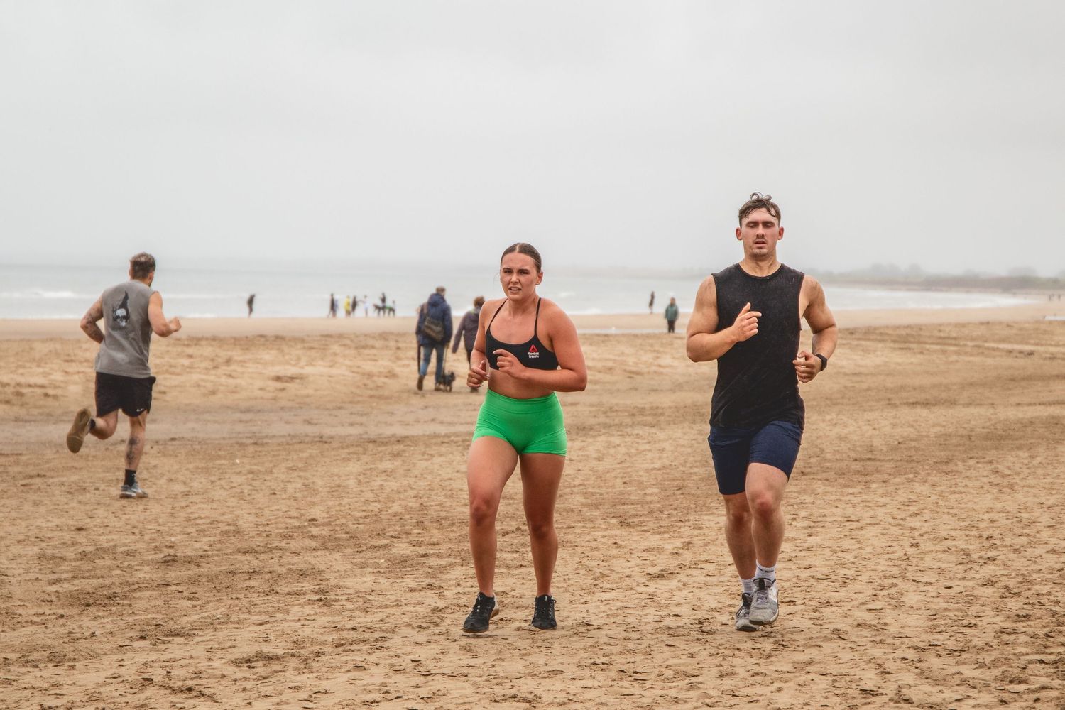 Group of people exercising on a sandy beach shore during an outdoor fitness class workout session.